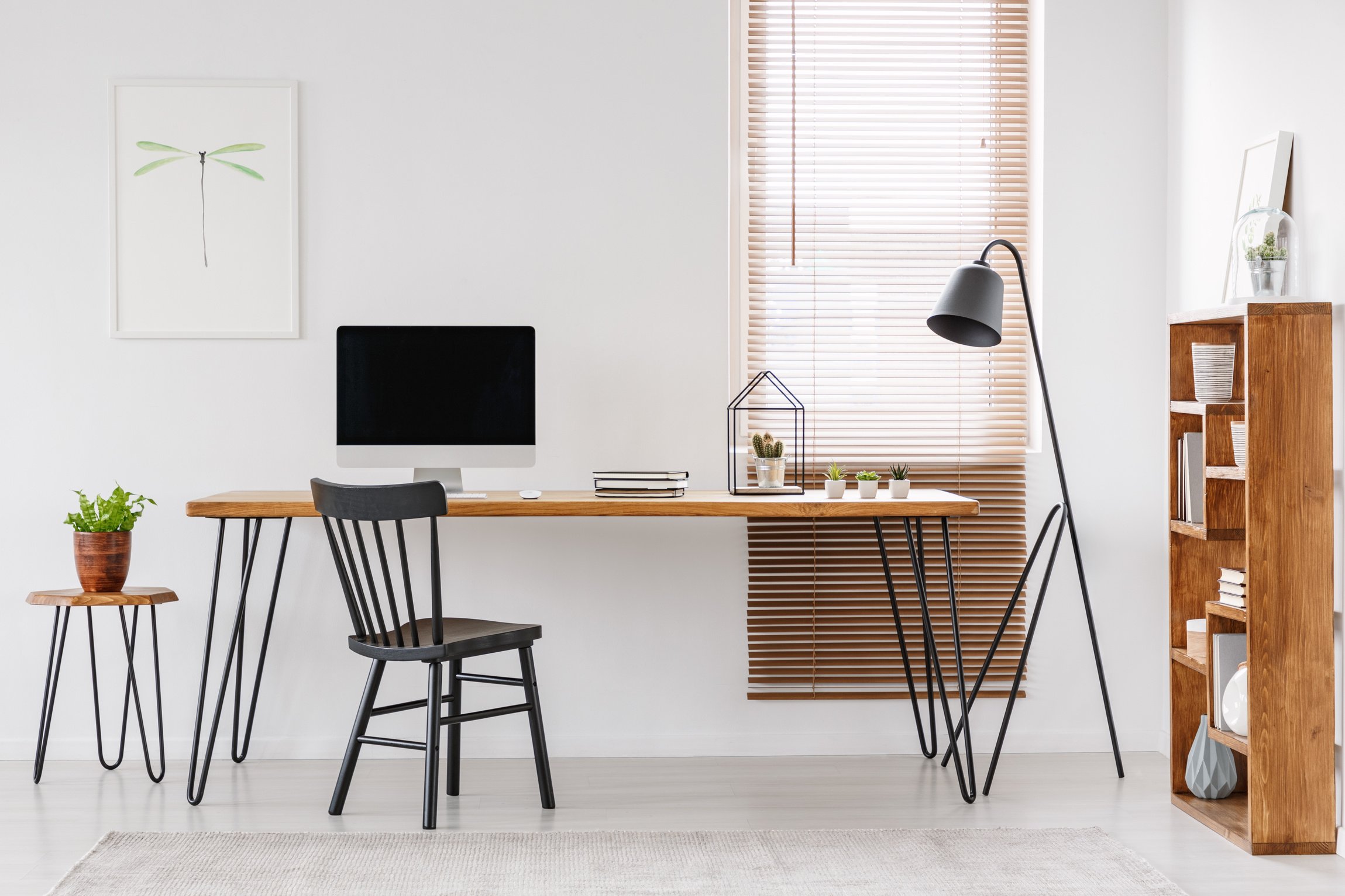Lamp next to wooden desk with computer monitor in home office interior with poster. Real photo